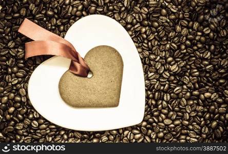 Coffee time concept. Heart shaped plate and cookie gingerbread with red robbon on coffee beans background. Top view