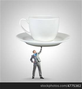 Coffee time. Young businessman lifting huge cup of coffee with one hand