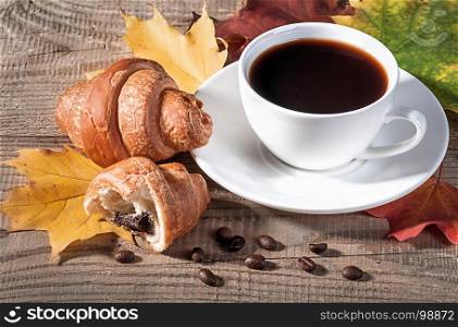 Coffee with a croissant on a wooden table. Grains of coffee and maple leaves on the table.