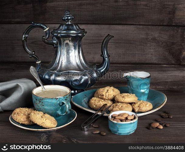 Coffee with cream in blue vintage cup, cookies and antique silver coffee pot on a old dark wooden boards