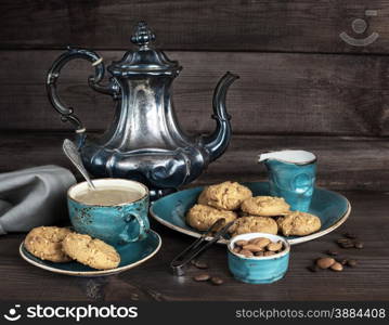 Coffee with cream in blue vintage cup, cookies and antique silver coffee pot on a old dark wooden boards