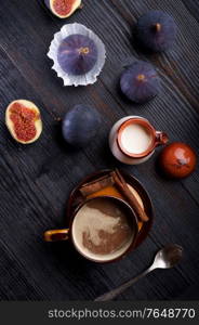 coffee with natural cream and tasty ripe purple fig on black wooden table. flat lay