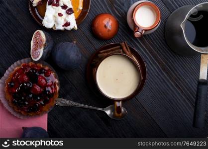 coffee with natural cream, piece of cake with berries and tasty ripe purple fig on black wooden table. flat lay. life style concept