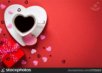 Coffee with red gift box and cookie in shape of heart. Composition for Valentines Day on red paper background. Top view. Copy space
