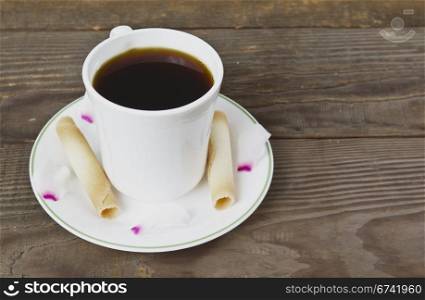Coffee with saucer, cup, flower petals and treats on wood