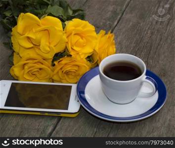 coffee, yellow roses and the mobile phone on a wooden table