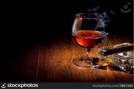Cognac and cigar on ashtray on a wooden table