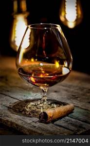 Cognac and cigar on old wooden table and a background of vintage lamps. Cognac and cigar