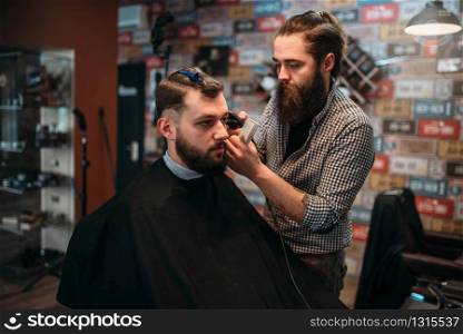 Coiffeur cutting hair of the client man in black salon cape. Barbershop concept