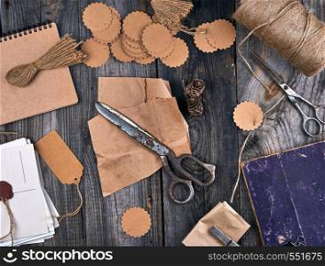 coil of brown rope, paper tags and old scissors on a gray wooden background, objects for making handicrafts