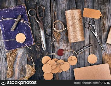 coil of brown rope, paper tags and old scissors on a gray wooden background, objects for making handicrafts