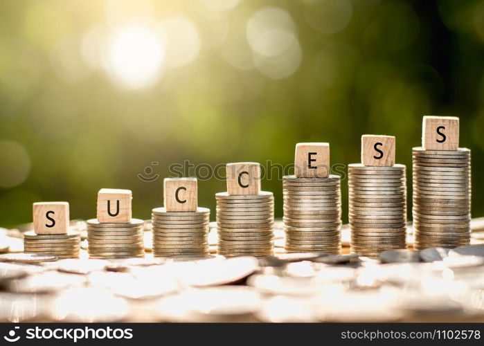 Coins stacked While there are wooden dice placed on the top along with the word success with morning sunlight shining.