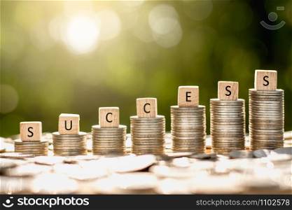 Coins stacked While there are wooden dice placed on the top along with the word success with morning sunlight shining.
