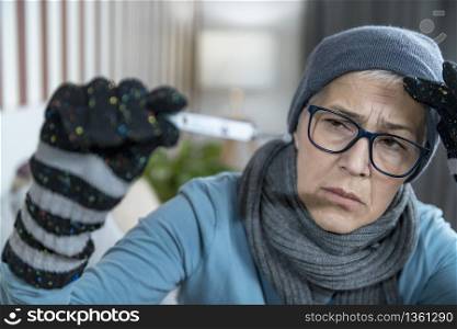 Cold and flu. Feverish Senior Older Woman reading her body temperature from digital thermometer. Cold and Flu. Senior Woman Looking at Digital Thermometer