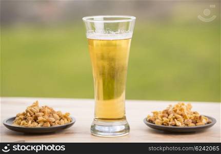 Cold beer with roasted peanuts, on wooden table, outdoor