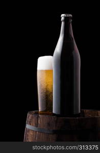 Cold bottle and glass of craft beer on old wooden barrel on black background