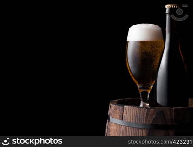 Cold bottle and glass of craft beer on old wooden barrel on black background