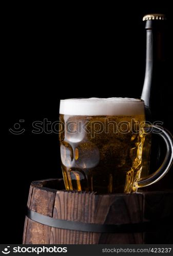 Cold bottle and glass of craft beer on old wooden barrel on black background