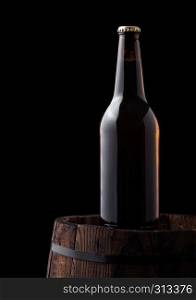 Cold bottle of craft beer on old wooden barrel on black background