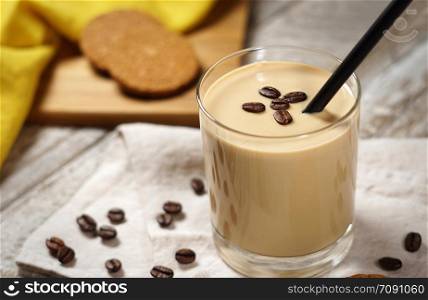 Cold coffee cream milkshake smoothie drink in a glass topped with coffee beans on a wooden rustic table.