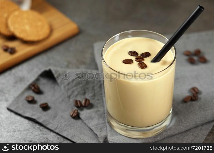 Cold coffee cream milkshake smoothie drink in a glass topped with coffee beans on a grey rustic table.