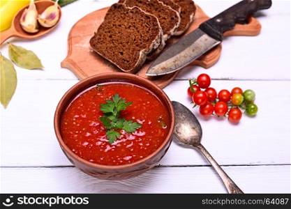 Cold creamy gazpacho soup of red tomato and fresh vegetables in a brown round plate, top view