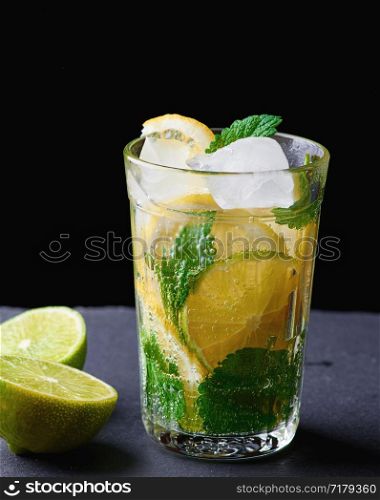 cold drink made from pieces of lemon, lime and leaves of green mint in a glass with water drops, next to ingredients for making lemonade