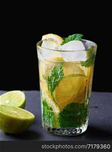 cold drink made from pieces of lemon, lime and leaves of green mint in a glass with water drops, next to ingredients for making lemonade