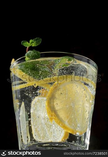 Cold drink on a black background. One glass with lemonade or mojito cocktail with lemon and mint. Close up