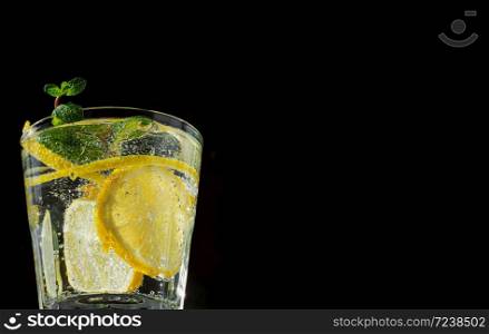 Cold drink on a black background. One glass with lemonade or mojito cocktail with lemon and mint. Close up, copy space