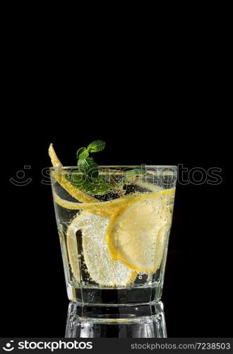 Cold drink on a black background. One glass with lemonade or mojito cocktail with lemon and mint. Copy space, close up.