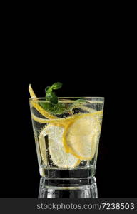 Cold drink on a black background. One glass with lemonade or mojito cocktail with lemon and mint. Copy space, close up.