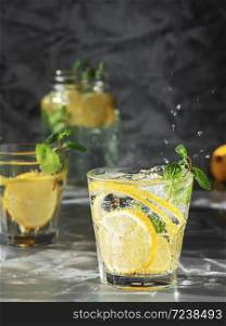 Cold drinks with splash or beverage with ice on dark background. Two glass with lemonade or mojito cocktail with lemon and mint. Copy space, close up