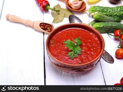 Cold gazpacho soup in a brown ceramic plate on a white wooden background, empty space on the left