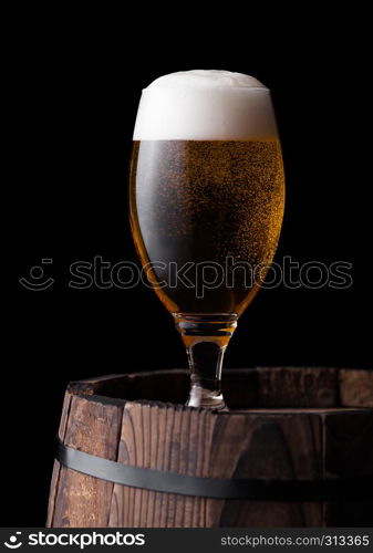 Cold glass of craft beer on old wooden barrel on black background