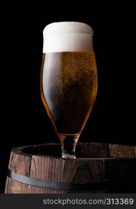 Cold glass of craft beer on old wooden barrel on black background