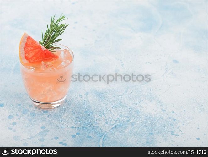 Cold grapefruit cocktail in glass with ice cubes and rosemary with grapefruits slice on blue background. Space for text