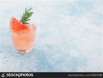 Cold grapefruit cocktail in glass with ice cubes and rosemary with grapefruits slice on blue background. Space for text