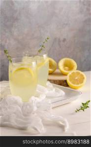 Cold lemonade or alcoholic cocktail with lemon, rosemary and ice in glass glasses on a light background.