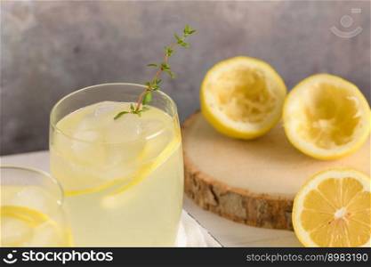 Cold lemonade or alcoholic cocktail with lemon, rosemary and ice in glass glasses on a light background.