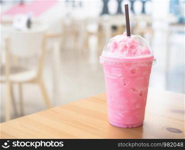 Cold milk smoothie in a plastic cup on a wooden table and has sunlight a beautiful background.