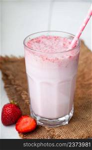 Cold milkshake with strawberries on a white background. Summer drink in a glass with a paper straw. Vertical photo. Cold milkshake with strawberries on white background. Summer drink in a glass with a paper straw.