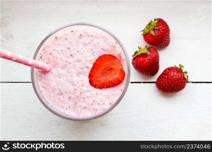 Cold milkshake with strawberries on a white background. Summer drink in a glass with a paper straw.. Cold milkshake with strawberries on white background. Summer drink in a glass with a paper straw.