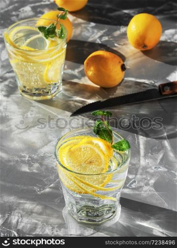 Cold refreshing drink or beverage with ice on dark background. Two glass with lemonade or mojito cocktail with lemon and mint. Copy space. Top view