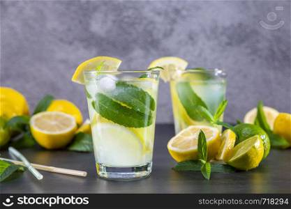 Cold refreshing summer lemonade with mint in a glass on a grey and black background. Focus on glass.