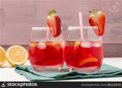Cold strawberry drink with fresh strawberries and lemon on wooden background