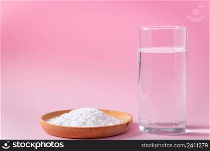 Collagen powder in wooden bowl and glass of water on pink background. Biological natural protein supplement to food. Skin and bone health. Anti-aging product. Place for your text.. Collagen powder in wooden bowl and glass of water on pink background. Biological natural protein supplement to food. Skin and bone health. Anti-aging product.