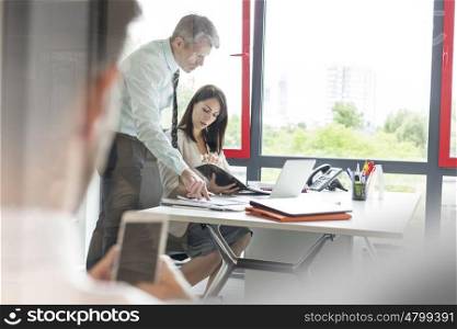 Colleagues over document at discussing at desk in office