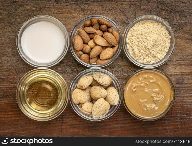 collection of almond super foods: nuts, flour, milk, oils and butter - top view of small glass bowls over rustic wood