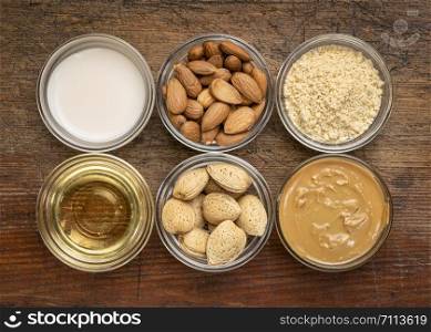 collection of almond super foods: nuts, flour, milk, oils and butter - top view of small glass bowls over rustic wood